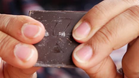 person breaking a piece of dark chocolate