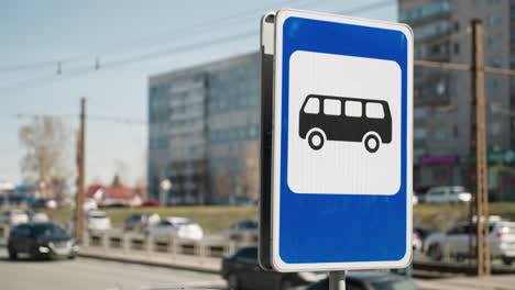 close view of a city bus stop sign on a sunny day with a busy road and buildings in the background