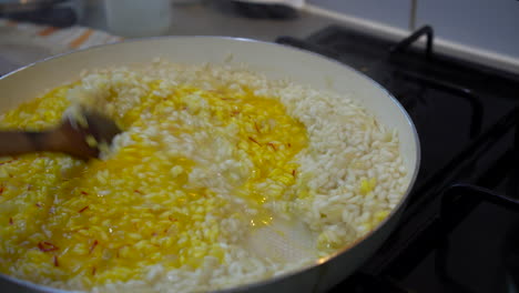 italian chef cooking yellow saffron risotto, stirring the saffron in the creamy rice