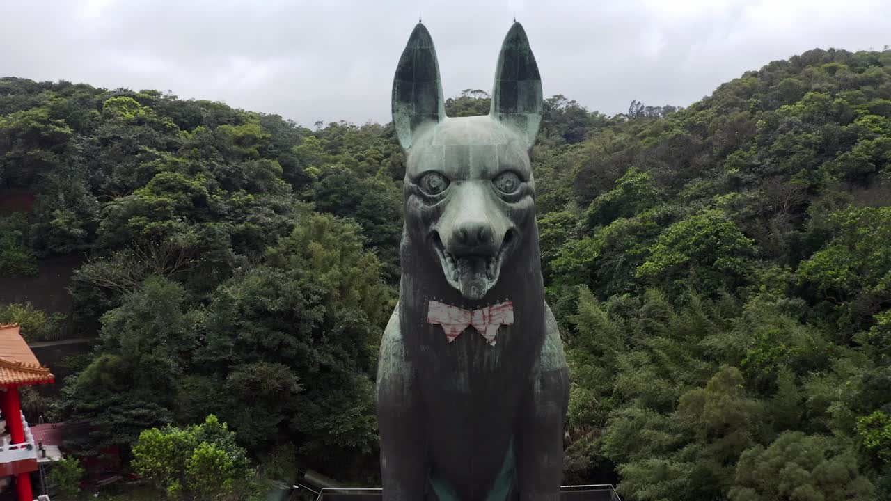 toma aérea cinematográfica hacia atrás que muestra una gigantesca estatua de perro al lado del templo asiático en taiwán rodeada de árboles verdes en las montañas