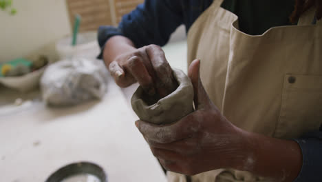 sección media de una alfarera que usa un delantal trabajando en arcilla para crear una olla en un estudio de cerámica
