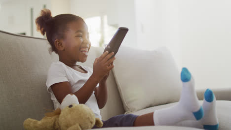 happy african american girl lying on sofa watching tv at home