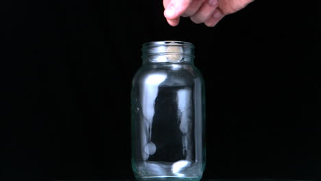 Hand-putting-two-euro-coin-into-glass-jar