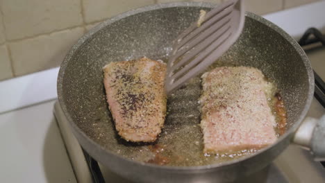 chef turn salmon fillet with poppy seeds cooking in olive oil on frying pan using spatula