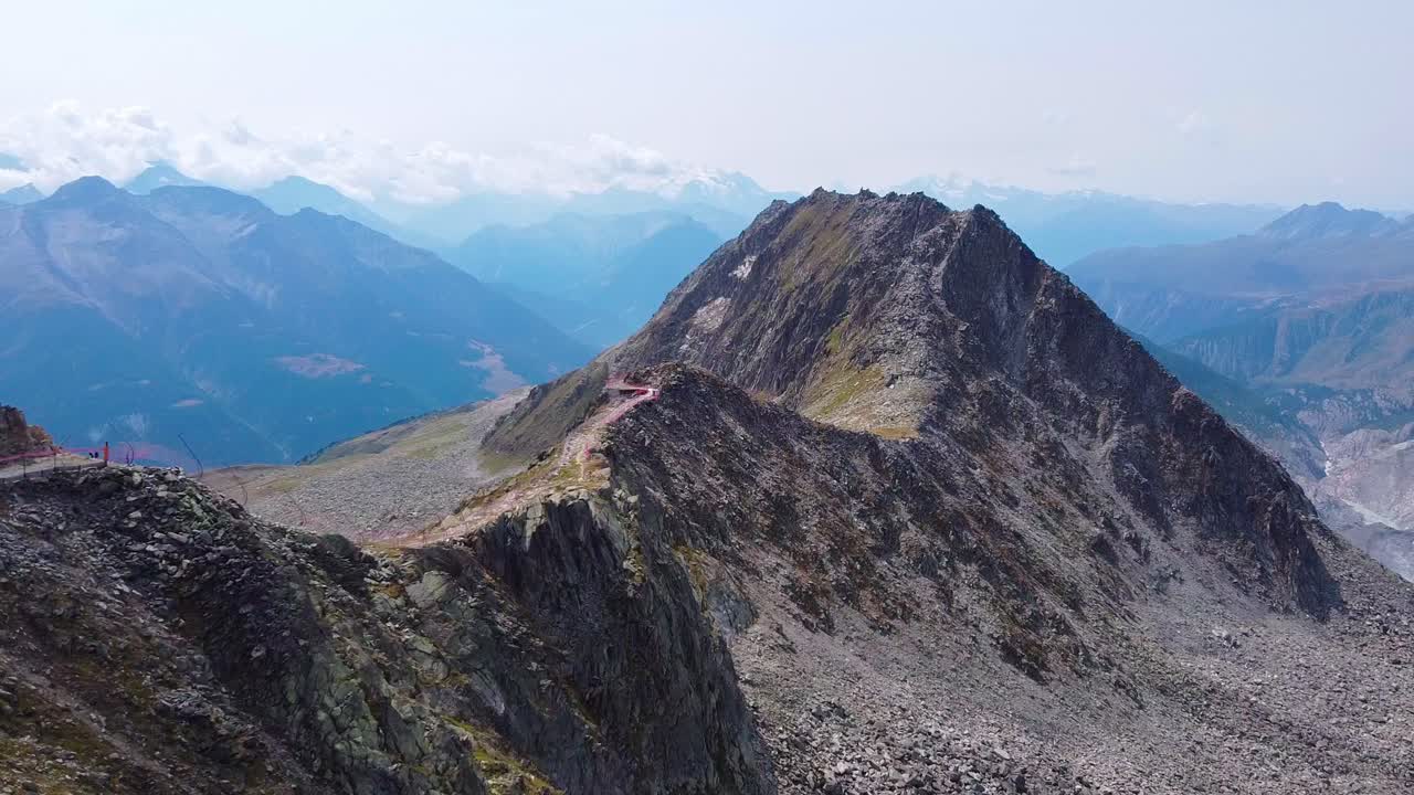 Aerial above Swiss Alps mountain range near the Aletsch glacier, rocky landscape with a hiking trail