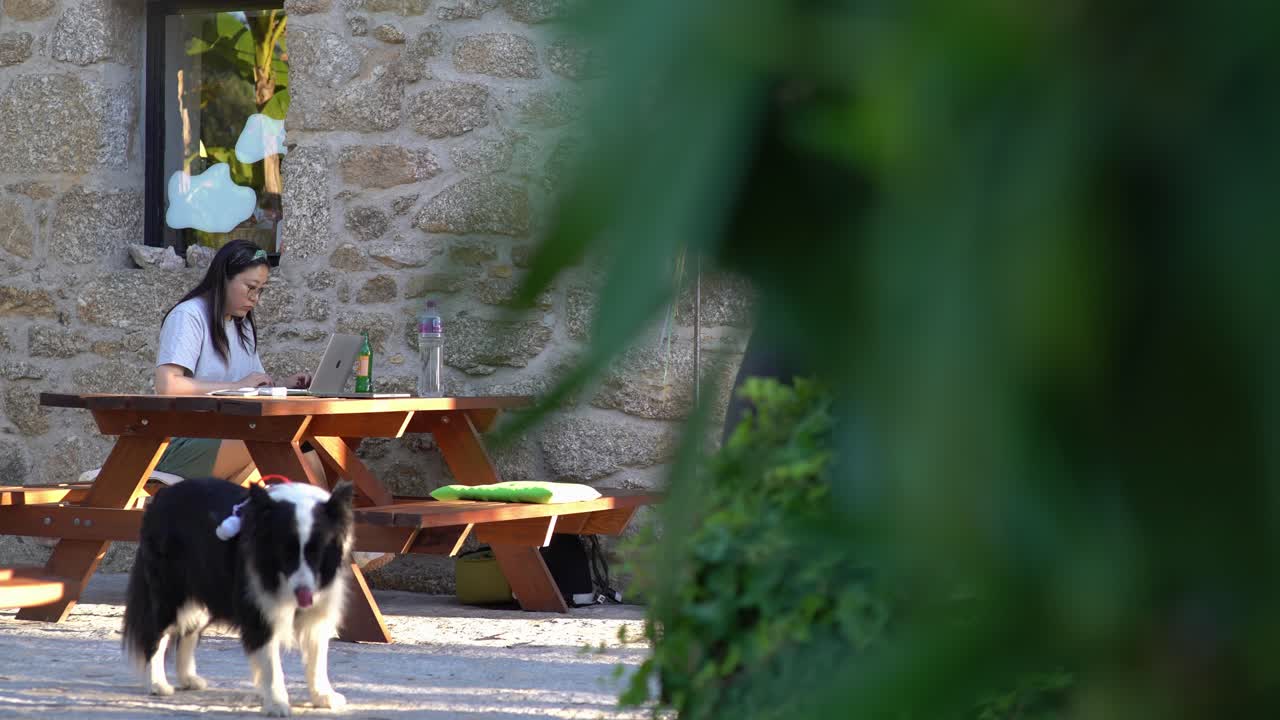 Una donna asiatica che usa un laptop davanti a una casa in pietra in un villaggio di montagna.