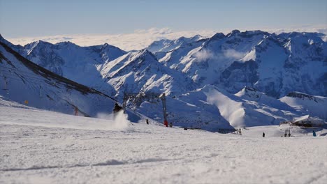 Nicht-Erkennbarer-Einzelner-Skifahrer,-Der-An-Einem-Sonnigen-Tag-Mit-Blauem-Himmel-An-Der-Kamera-Vorbeifährt-Und-Schnee-Mit-Blick-Auf-Die-Berge-Sprüht