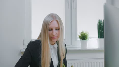 beautiful business woman concentrating on work. attractive young blond female in elegant jacket sitting with pen and notebook at desk with computer and looking excitedly at monitor screen.