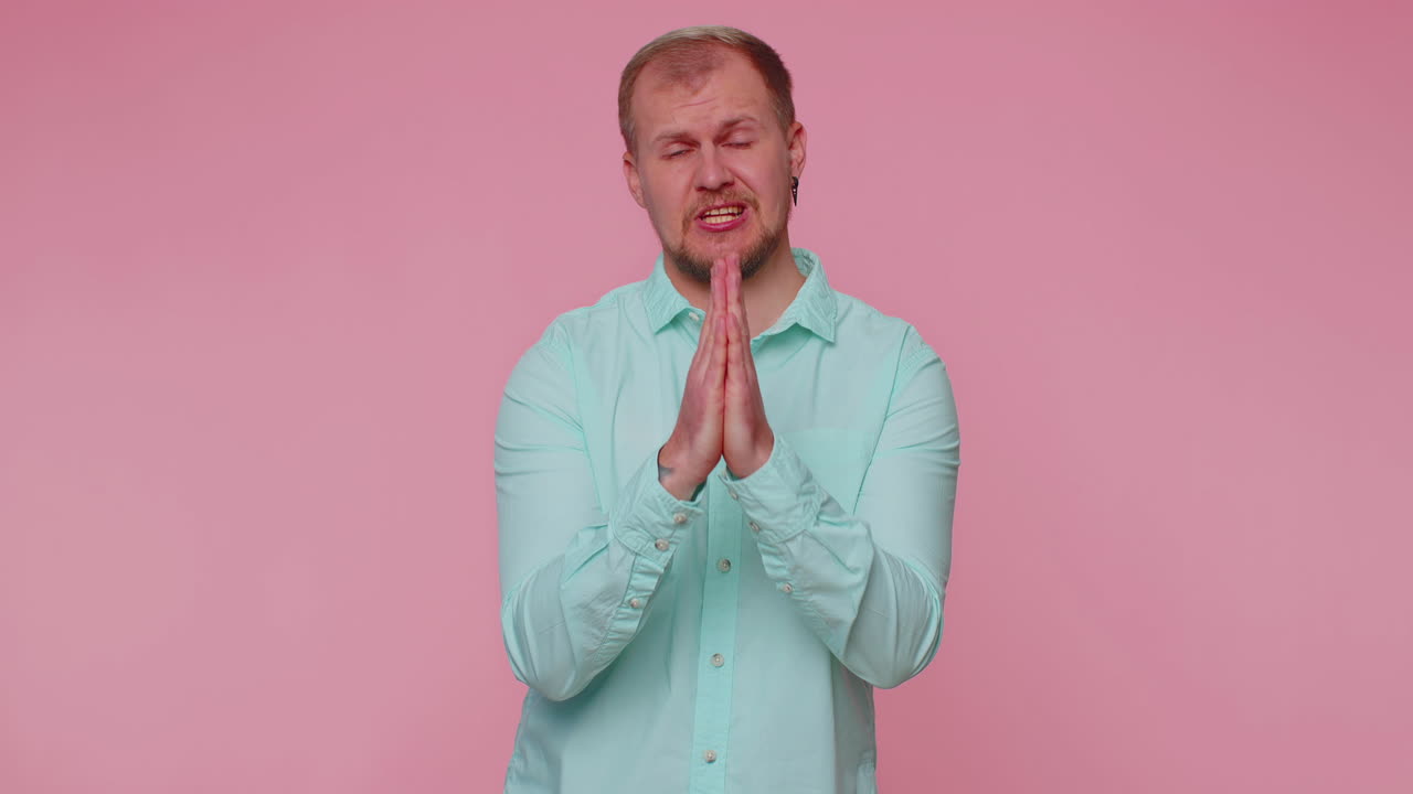 Trendy young adult man praying, looking upward and making wish, asking God for help, begging apology