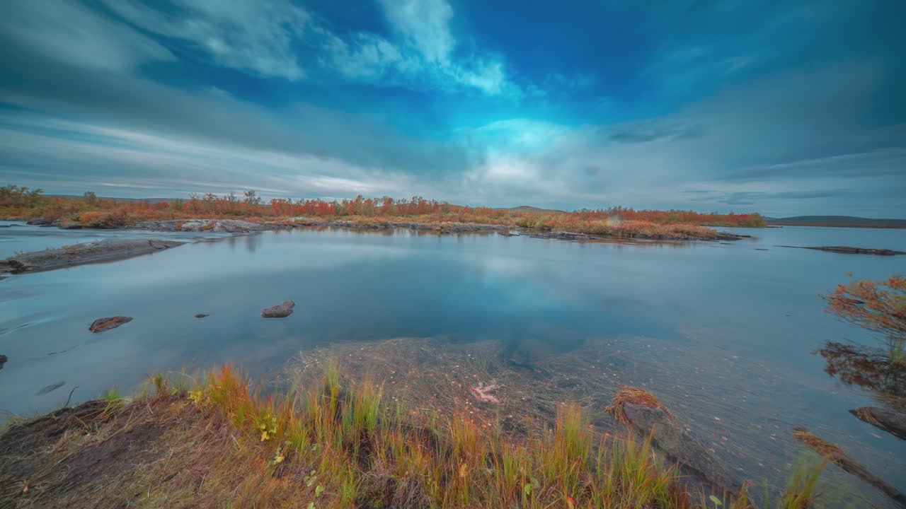 Fast-moving clouds move in the sky above the shallow river with forest-covered banks flowing through the Finnish tundra