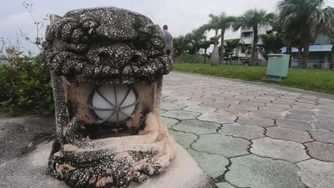 obese white man walks past shisa dog statue in a public park