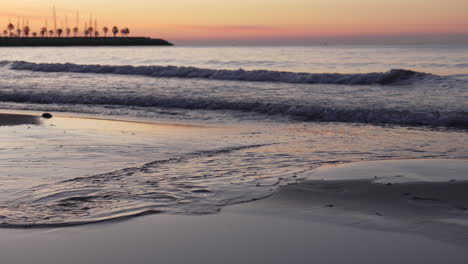 sunrise-skyline-is-reflected-in-coastal-waters-that-wash-up-onshore-as-a-man-walks-across-leaving-footprints-in-sand