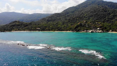 Vista-Aérea-Baja-Sobre-El-Mar,-En-La-Costa-Del-Parque-Natural-Nacional-Tayrona,-Día-Soleado,-En-El-Caribe-Colombia,-Sudamérica---Seguimiento,-Pan,-Disparo-De-Drones