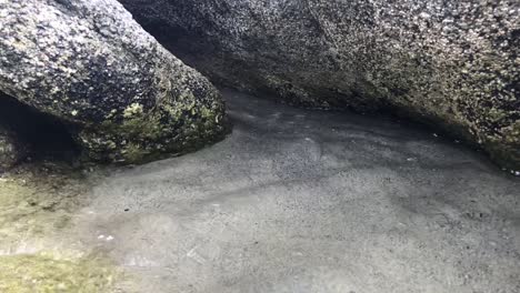 Cámara-Lenta-De-La-Marea-Alta-Entrante-Entre-Dos-Grandes-Rocas-En-El-Fondo-Marino-Arenoso