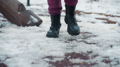 leg view of person in black boots jogging in outdoor park in urban setting, cold weather, snow on ground, fitness in winter, exercising outside during chilly day, park playground visible