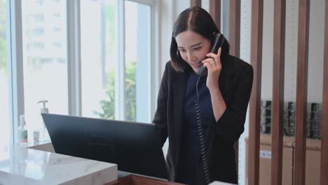 asian hotel receptionist woman receive phone call for room reservation then look at camera and smile