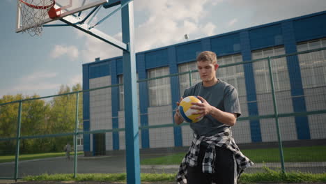 volleyball player during training session bouncing volleyball, rotating it in hand before throwing and slamming it, captured outdoors in sports arena with basketball court in background