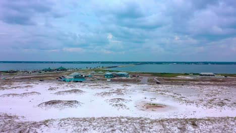 Drone-view-flying-over-the-white-sand-of-Navarre-Beach-Fl-looking-towards-the-calm-waters-of-the-sound-bay-with-a-view-of-the-bridge-and-board-walk