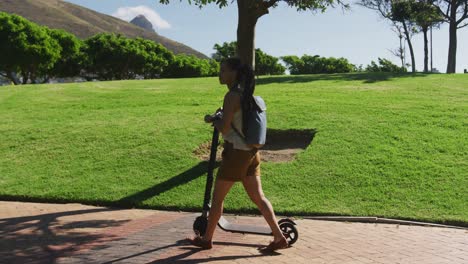 African-american-woman-wearing-backpack-riding-scooter-in-park
