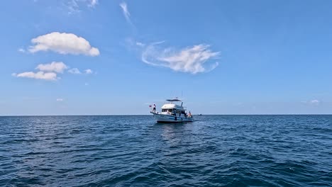 a fishing boat with a person aboard moves steadily toward the camera across calm ocean waters under bright daylight and clear blue sky