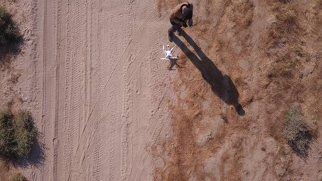 young man prepares to launch white drone from dry sand road in desert