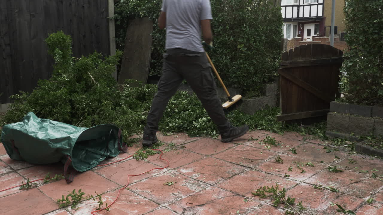 macho adulto asiático del reino unido usando una escoba de jardín para barrer los recortes de cobertura en el jardín delantero