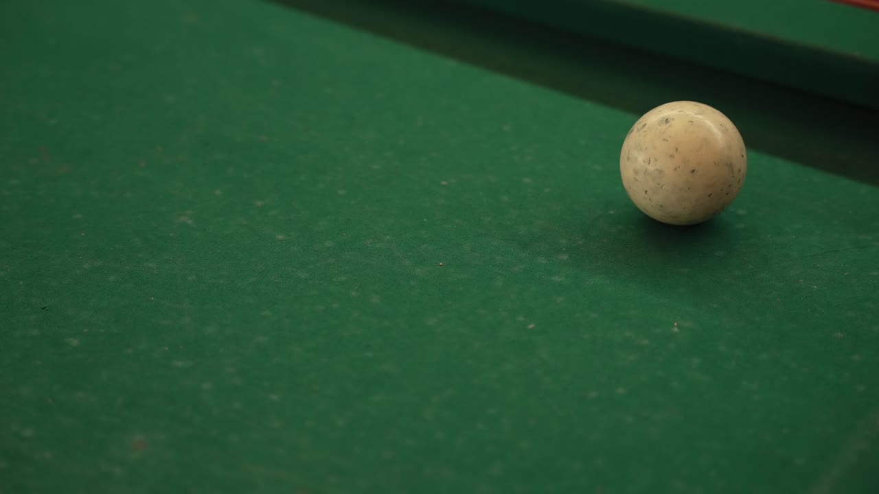 Taco de billar se acerca a la bola blanca en una mesa de billar verde justo antes de golpear.