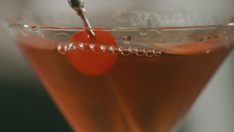 close-up of an elegant martini glass with a carefully placed metal toothpick, garnished with a cherry.