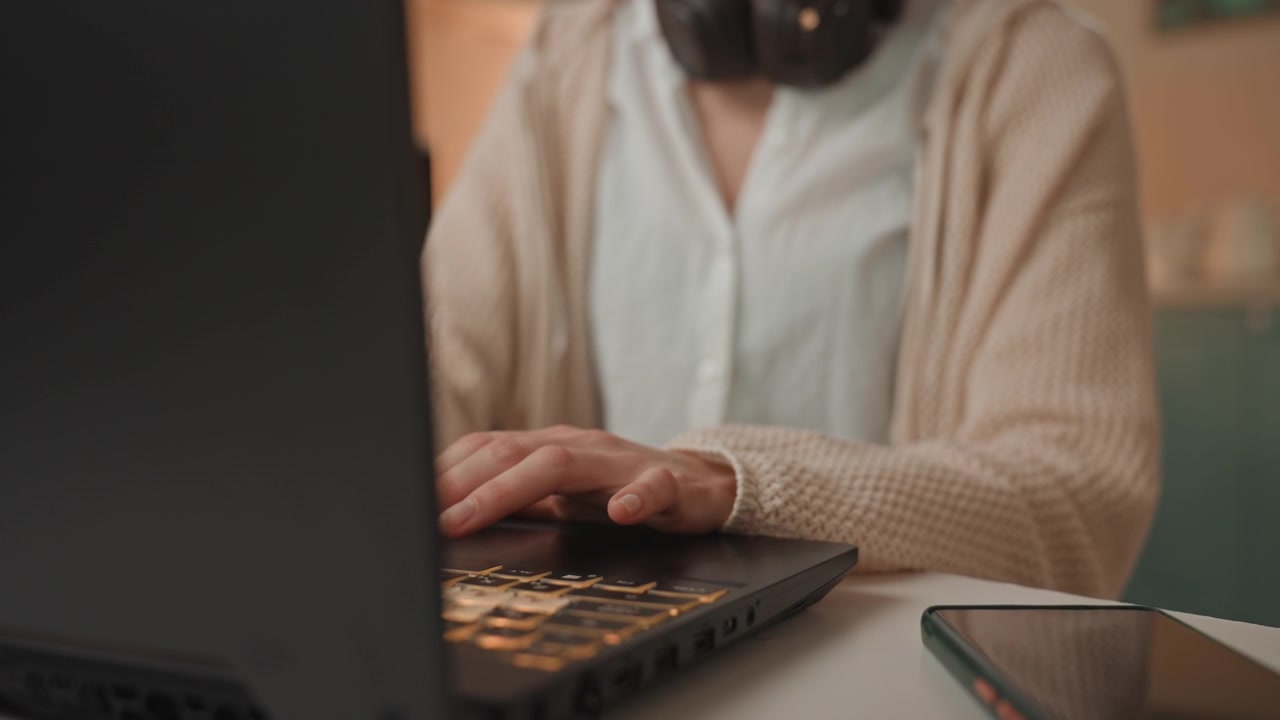Hvid kvinde, musikelsker, taster. Farverigt baggrundsbelyst tastatur, hovedtelefoner om halsen, hyggelig sweater, nærbillede af hænder, smartphone på skrivebordet, stille aften i hjemmestudie, fokuseret kreativt workflow, mix.