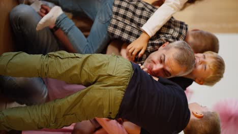 Vertical-video-of-happy-children-hugging-their-teacher,-a-man-with-gray-hair-in-a-purple-T-shirt-in-a-club-for-preparing-children-for-school