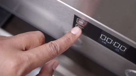 close-up of a hand pressing a button on an oven control panel