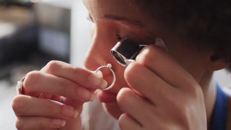 trabajadora biracial inspeccionando un anillo con lupa en un taller en cámara lenta