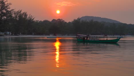 green-wooden-boat-at-anchor-off-the-beach,-gently-moving-on-small-waves