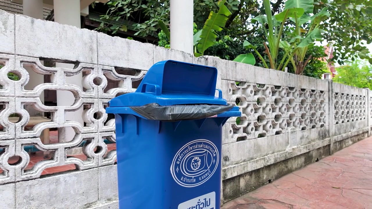 Contenedor azul de residuos generales al aire libre contra una pared de hormigón decorativa