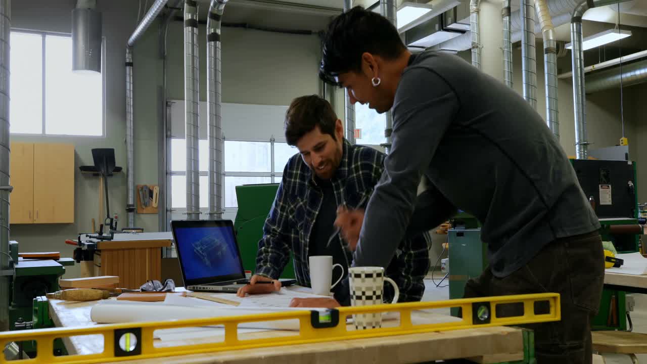 Carpenters discussing on blueprint in workshop 4k