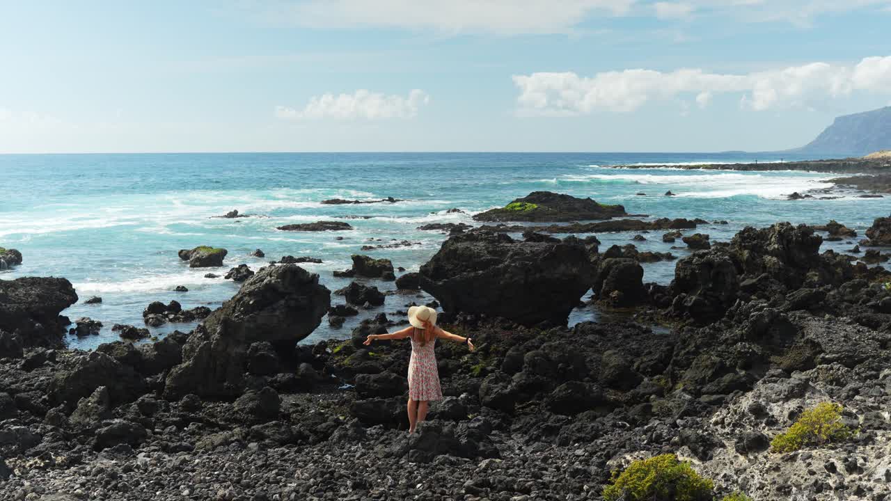 아름다운 젊은 여성은 테네리페 섬의 해안 바위, 뒷면을 즐기고 있습니다.