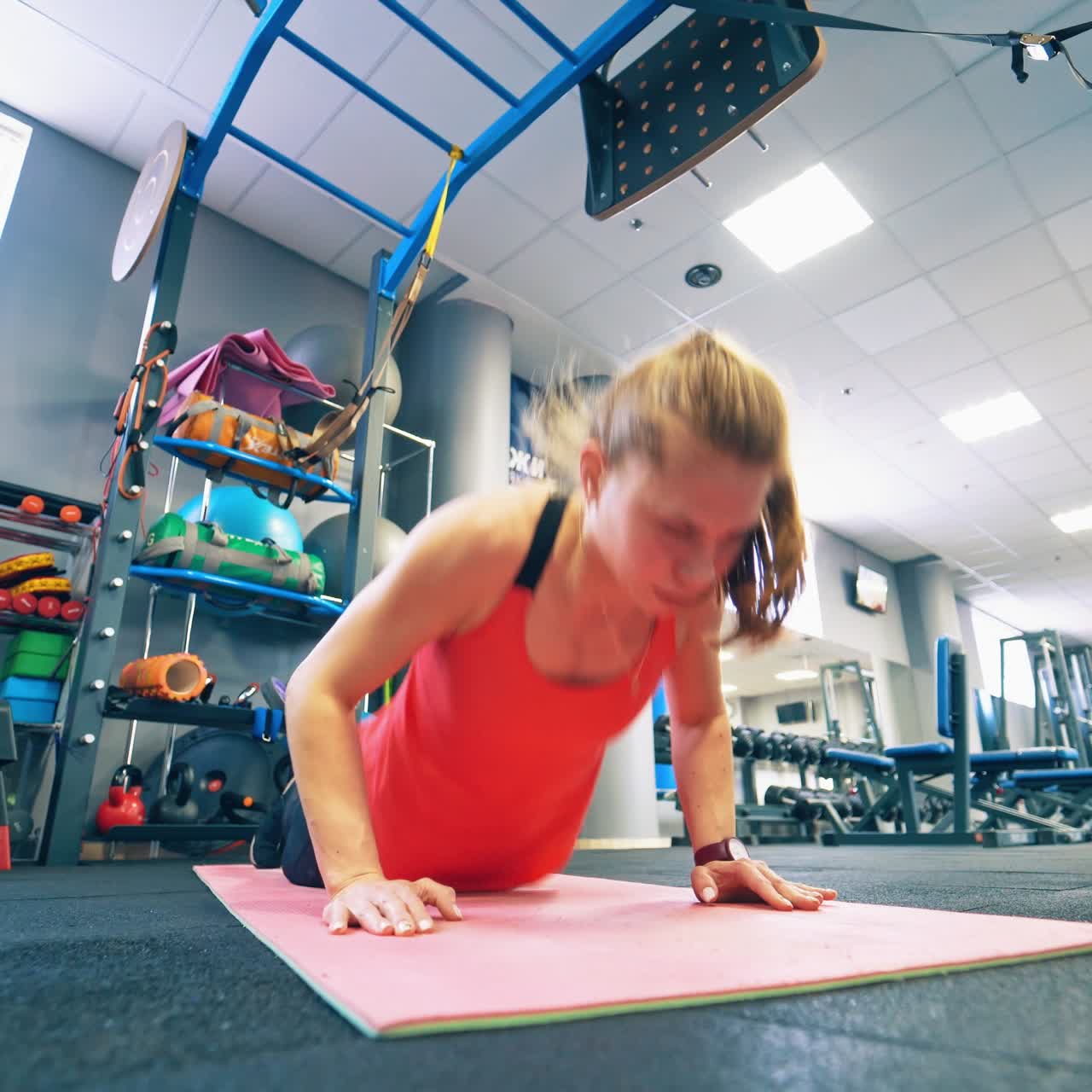 Beautiful girl doing exercises on a mat. Young woman in sportswear doing push-ups workout in the modern fitness centre.