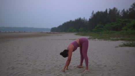 Joven-India-Haciendo-Estiramientos-De-Rutina-De-Yoga-En-La-Arena-De-La-Playa-Al-Atardecer,-Amanecer