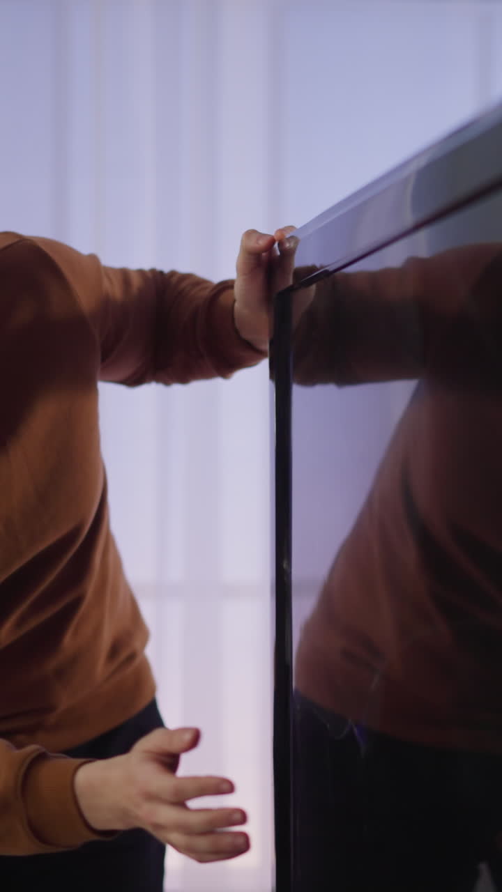 hombre confundido golpea la pantalla de la televisión inteligente con trincheras contra las cortinas de la ventana en el apartamento en cámara lenta. hipster y televisor roto en casa. electrodoméstico dañado