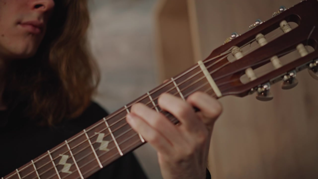 Closeup classical guitar hands playing in studio lesson wooden nylonstring guitar rosette and fretboard visible, longhaired musician demonstrating fingerstyle technique, slow precise plucks, warm