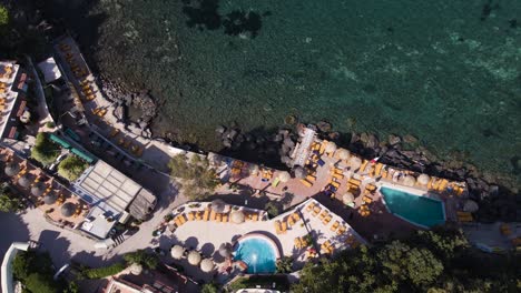 Downward-panning-drone-shot-revealing-a-resort-on-the-coastline-of-the-tropical-island-of-Ischia-located-near-Naples-in-Italy