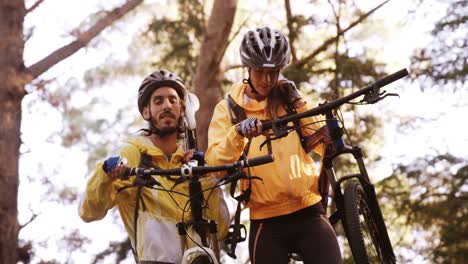 pareja de ciclismo de montaña llevando una bicicleta e interactuando entre sí