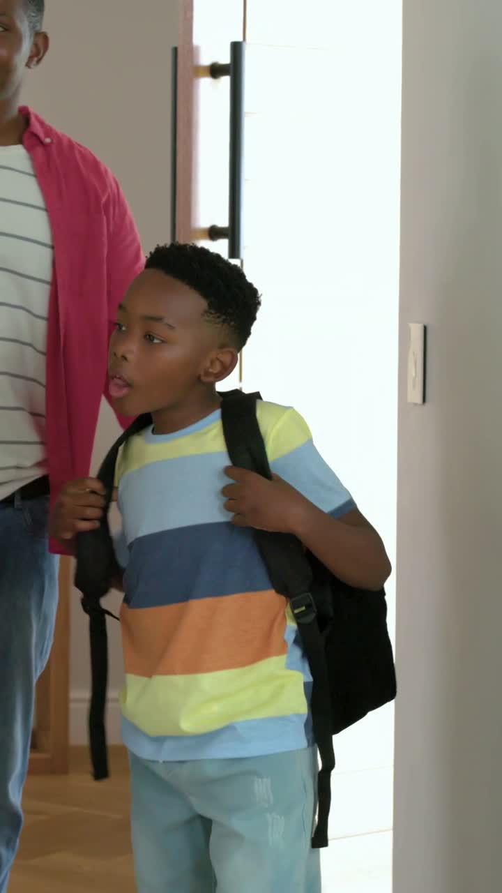 Vertical video: Opening wood door, father guiding boy coming home into entry, fixing black backpack