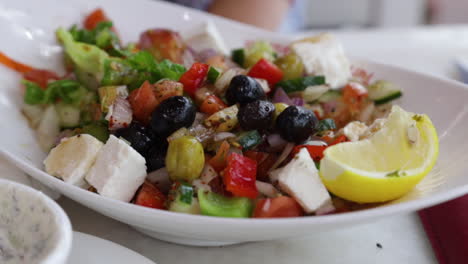 person eating a fresh dish of greek salad at a restaurant table, close up shot.
