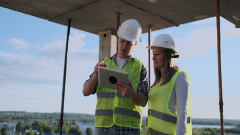 trabajador de la construcción hombre y arquitecto mujer en un casco discutir el plan de construcción de la casa hablar el uno al otro sobre el diseño sosteniendo una tableta mirar los dibujos fondo de los rayos del sol.