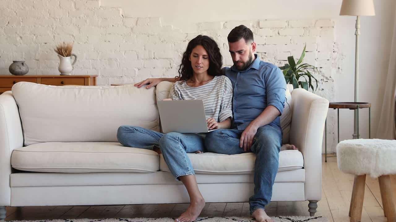 Couple relaxing on couch with laptop, talking discussing purchase on-line