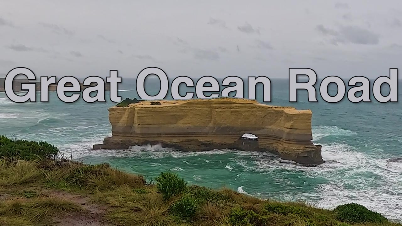 Une grande cheminée de fée en grès avec une arche naturelle se dresse au large le long d'une côte accidentée de la Great Ocean Road par une journée couverte. Great Ocean Road
