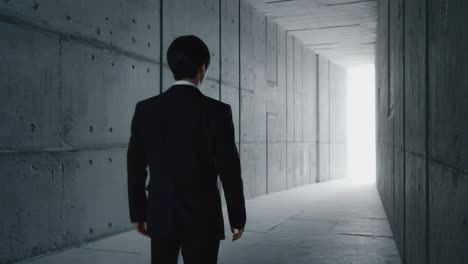 a man in a suit walks through a concrete tunnel towards a bright light