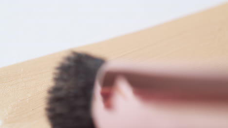 Close-up-of-brushing-from-left-to-right-of-a-make-up-nude-colored-foundation-on-a-clean,-white-board-with-a-small-wand-applicator