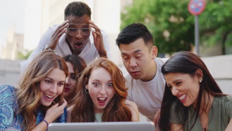 diverse group of friends reacting with shock and amusement to content on a laptop outdoors